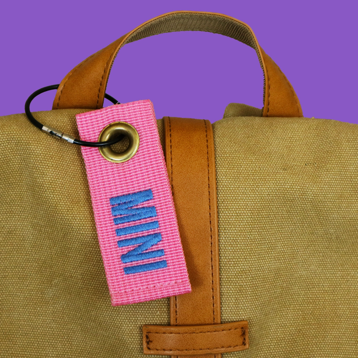 Pink mini bag tag embroidered MINI, hanging from a canvas bag handle on a black wire keyring